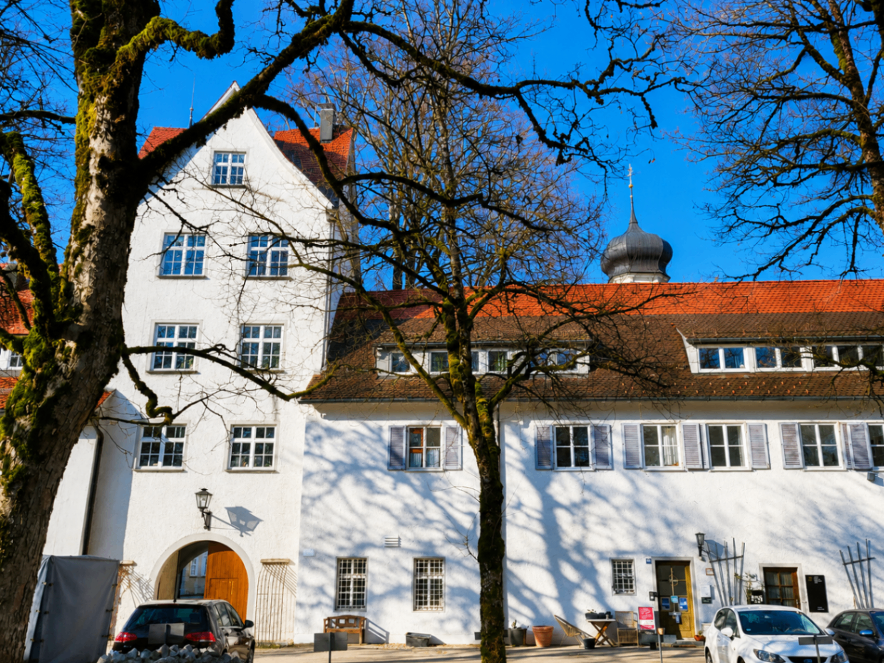 Schloss Isny mit Zwiebelturm hinter kahlen Baumkronen im Frühjahrslicht